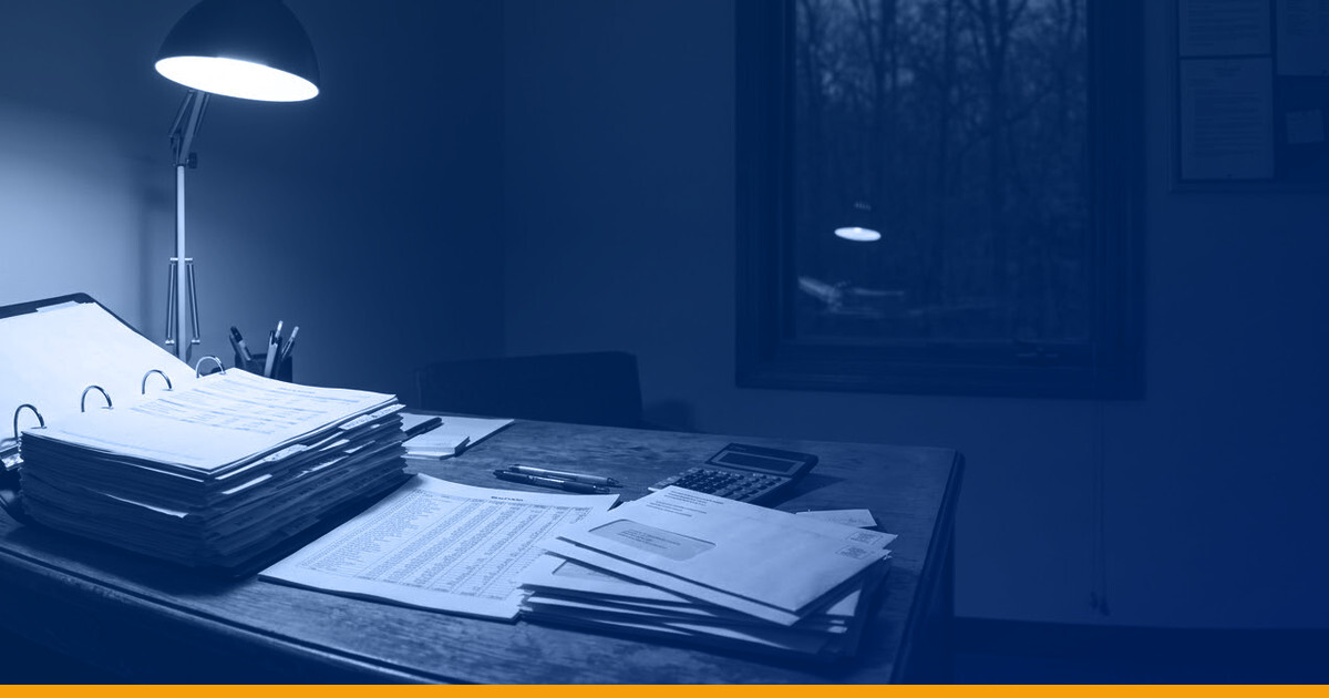 A property management desk at night: a thick budget binder, a printed rent roll and a stack of tenant estimate letters under a single desk lamp, with a dark window behind, under a Kardin navy gradient overlay.