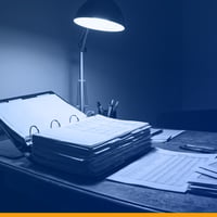 A property management desk at night: a thick budget binder and a printed rent roll under a single desk lamp, under a Kardin navy gradient overlay.